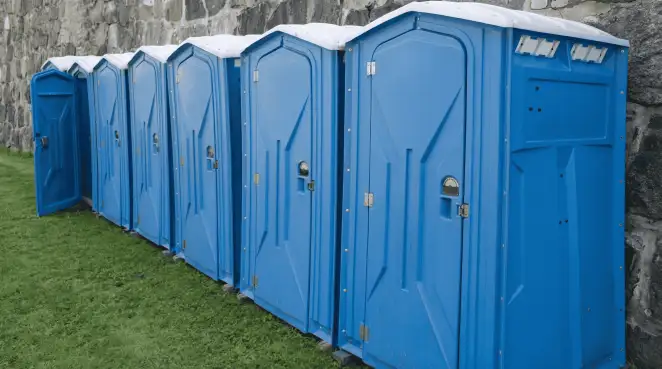 Row of blue portable toilets lined up on grass against a stone wall for event sanitation in Pittsburgh, PA
