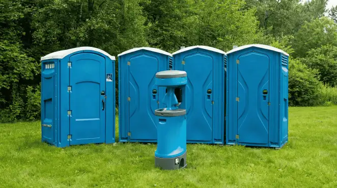 Four blue portable toilets and a matching hand washing station on grass near trees, a common sight at local outdoor events in Pittsburgh, PA