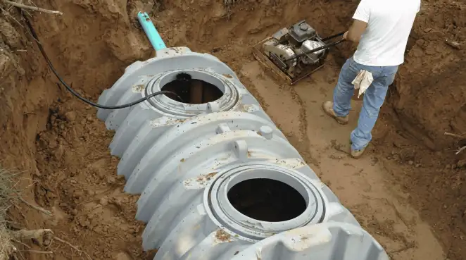Septic tank installation showing a technician compacting soil around a new poly septic tank in an excavation pit in Pittsburgh, PA